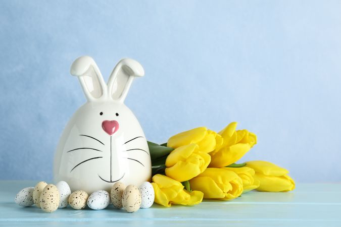 Decorated bunny and Easter eggs on table against color background. Space for text