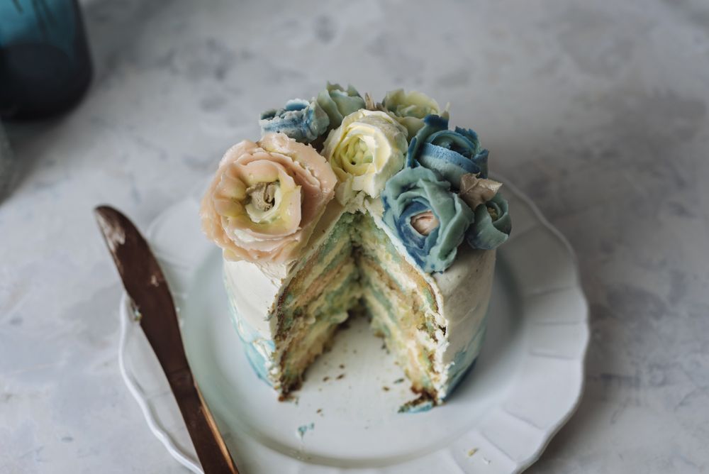 Portion of rainbow cake, filled with chantilly cream, and decorated with buttercream flowers
