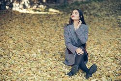 Female sitting relaxing in park in fall time with colorful leaves on ground