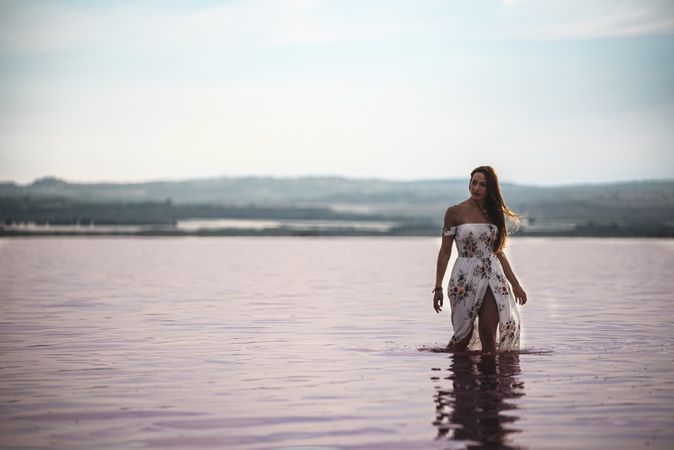 Peaceful woman in white dress walking ankle deep in pink lake
