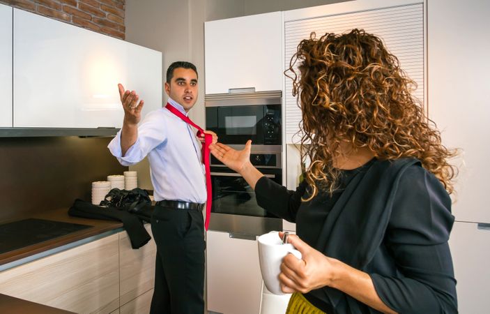 Man arguing with curly haired woman at home while knotting his tie