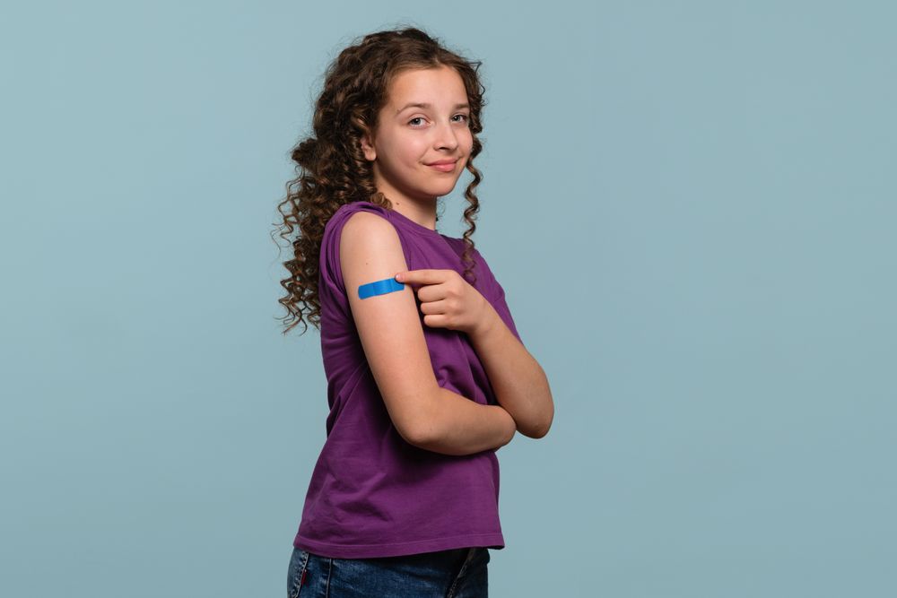 Girl pointing at bandage on arm after receiving vaccine