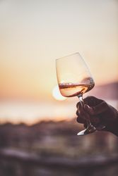 Man's hand holding glass of rose wine against sunset, vertical composition