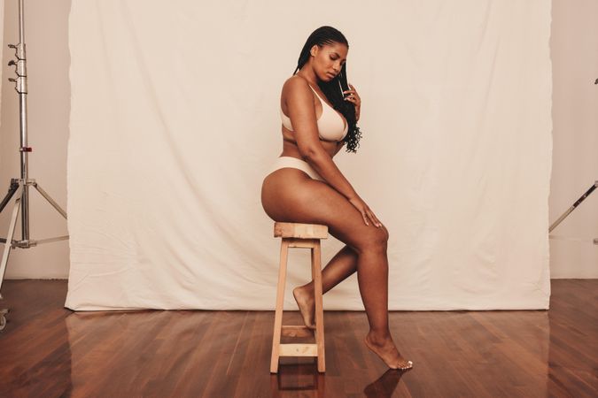 Side view of body positive young woman sitting on a stool in photo studio