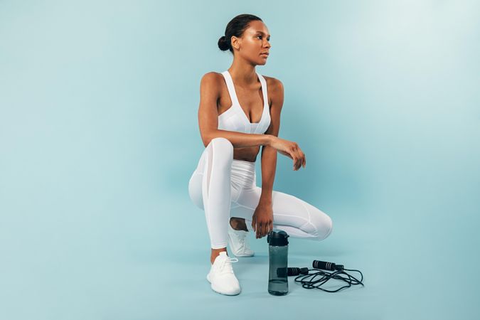 Woman kneeling in blue studio after working out with jump rope and water bottle