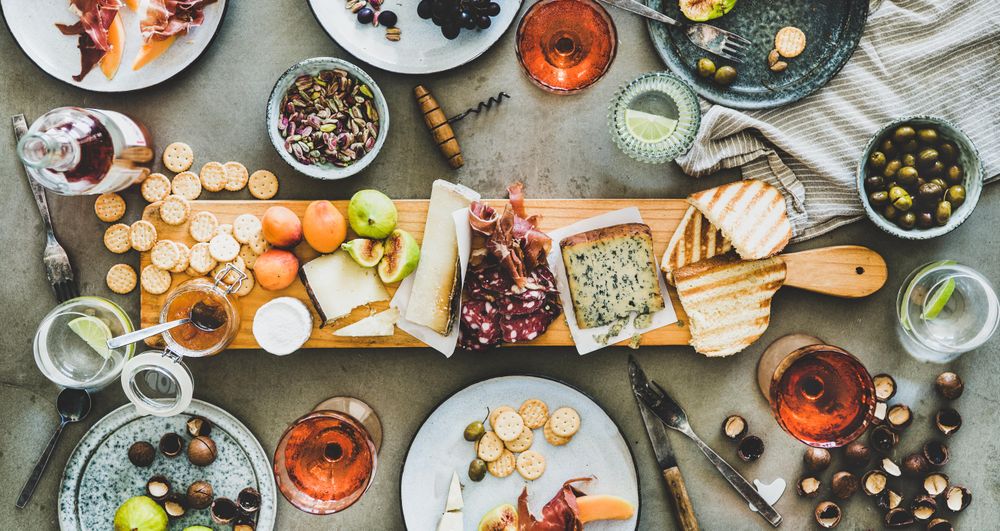 Charcuterie board with rose wine, hazelnuts, crackers, cheese, prosciutto, melon, wide composition