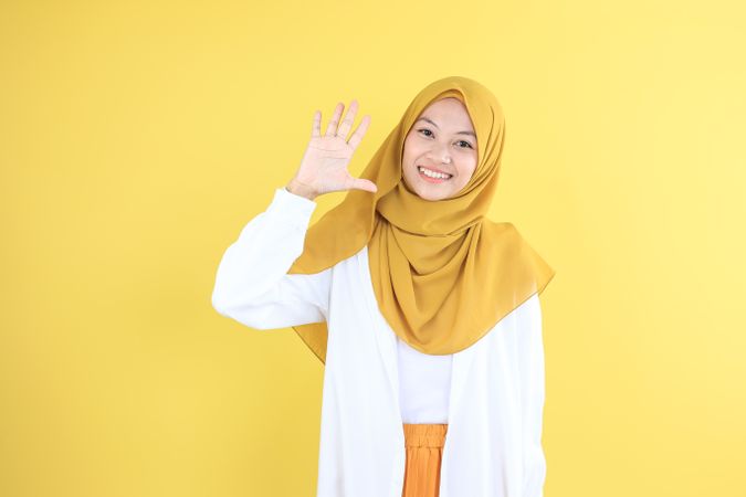 Asian Young Muslim Woman in Mustard Veil and Shirt Waving Hand Say Hi or Goodbye