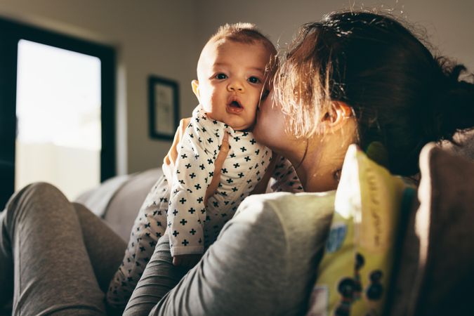 Young mother kissing her baby sitting on a couch at home