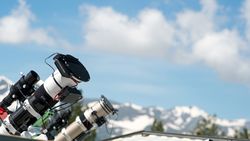 Telescopes on observatory rooftop with mountain view.