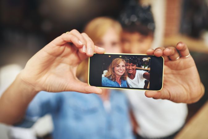 Two female friends pictured through a smart phone screen taking a selfie