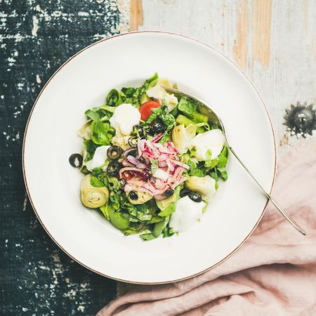 Artichoke salad in bowl, on blue painted wooden background, square crop