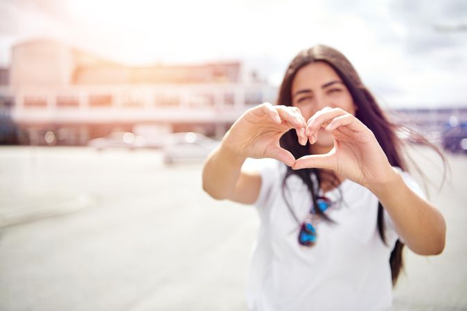 Woman making heart sign with hands standing in street outside