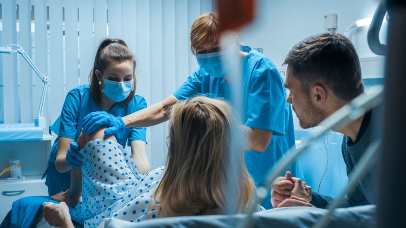 Emergency In the Hospital: Woman Giving Birth, Husband Holds Her Hand in Support, Obstetricians Assisting