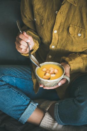 Woman in jeans about to eat from cup of squash soup