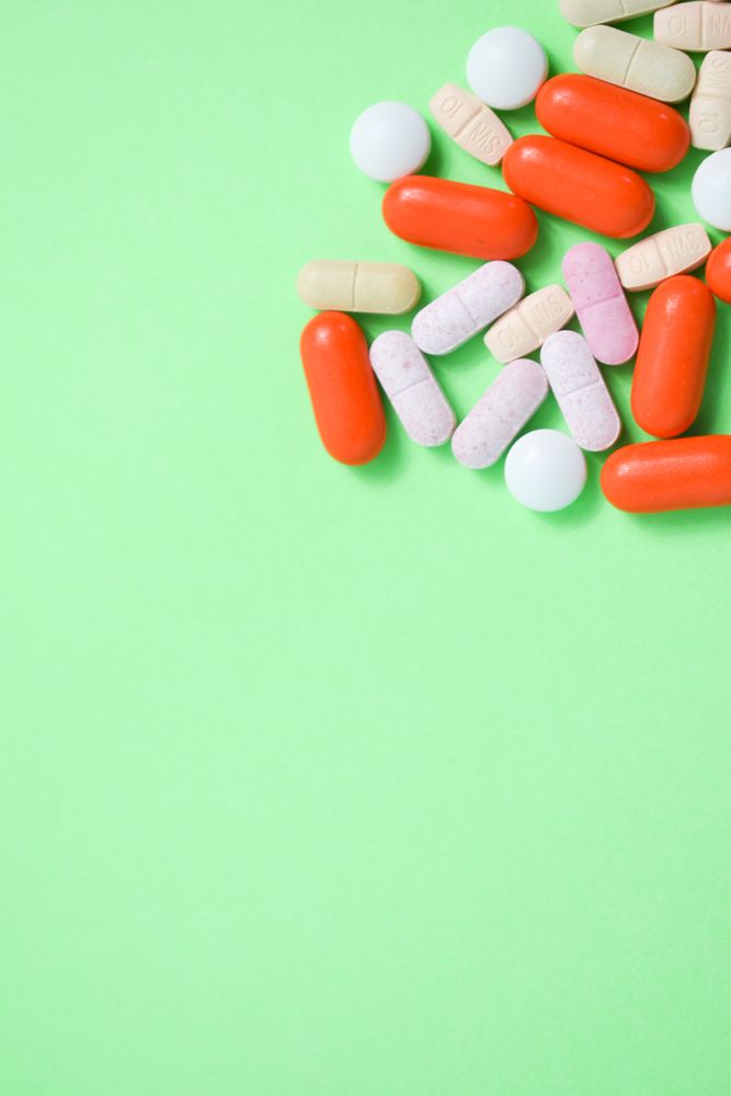 Top view of variety of prescription medication and vitamins on green table with copy space