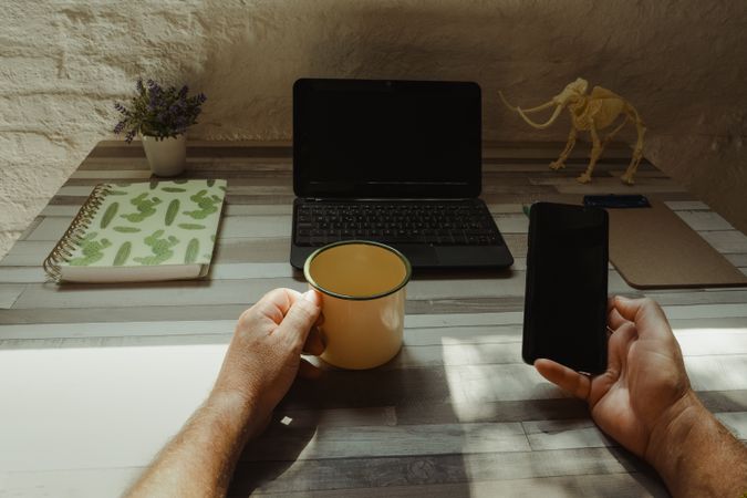 Crop freelancer with mug using smartphone