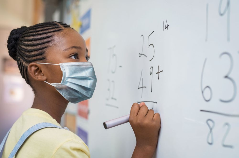 Teenage girl with facemask solving math problem on light board