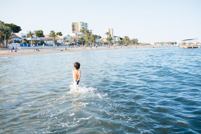 Boy walking in blue water of resort sea