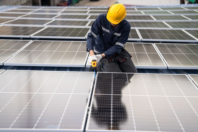 Engineer worker using electric drill repairing on solar cell panel on the roof of the factory. After service and security for industrial renewable energy concept