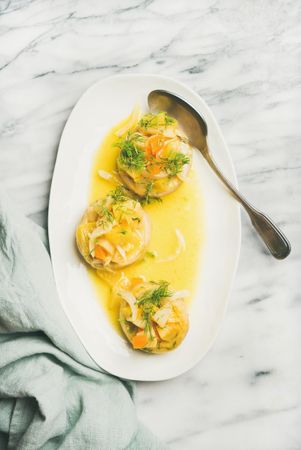 Artichoke hearts with orange sauce and silver serving spoon on marble background