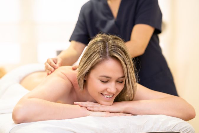 Happy blonde female having shoulders massaged on the table
