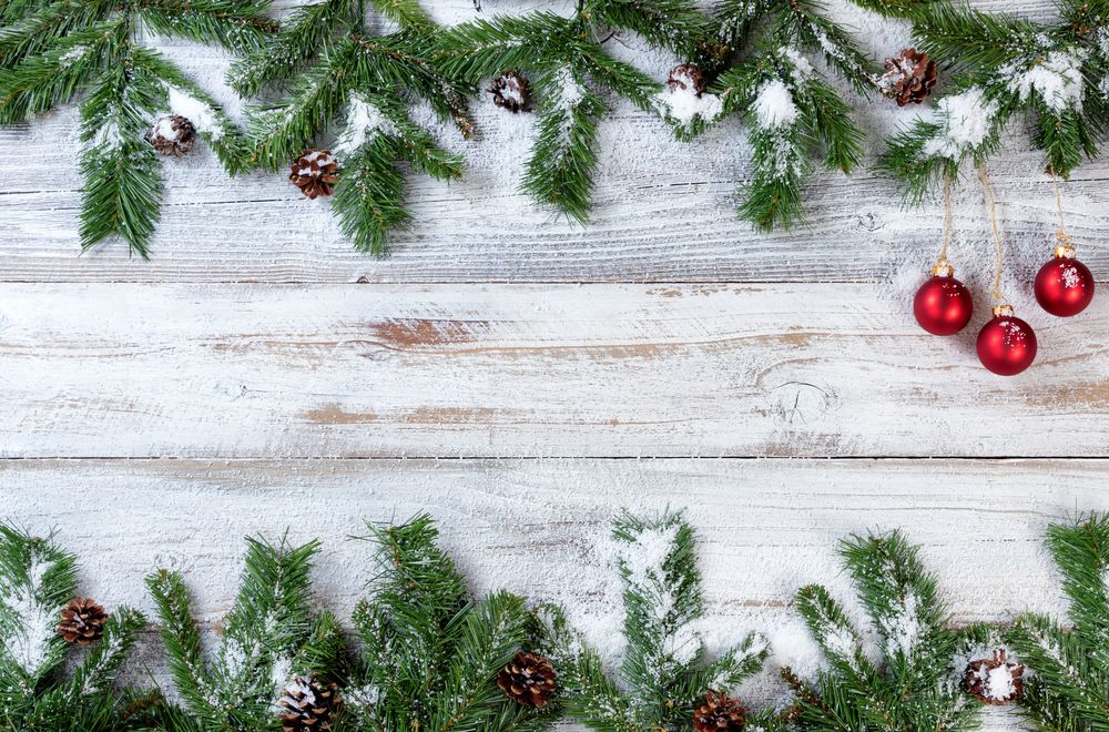 Snowy Christmas branches with red ornaments on rustic wooden background