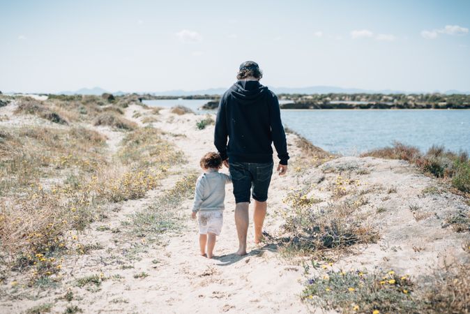 Man with kid walking along sandy hilly seaside