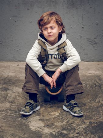 Cute kid sitting on skateboard on street