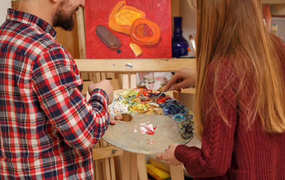 Back of male and female in front of easel with palette