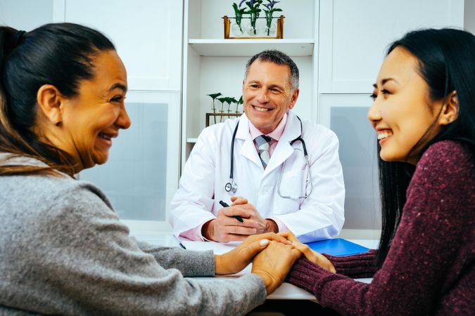Happy doctor sharing news with two smiling patients in medical office