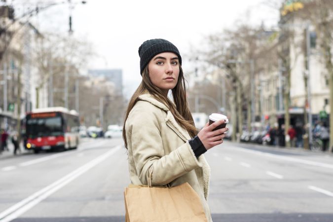 Portrait of female crossing the street, with takeaway coffee and shopping bag