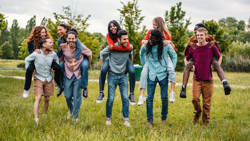 Friends piggy backing together in green park