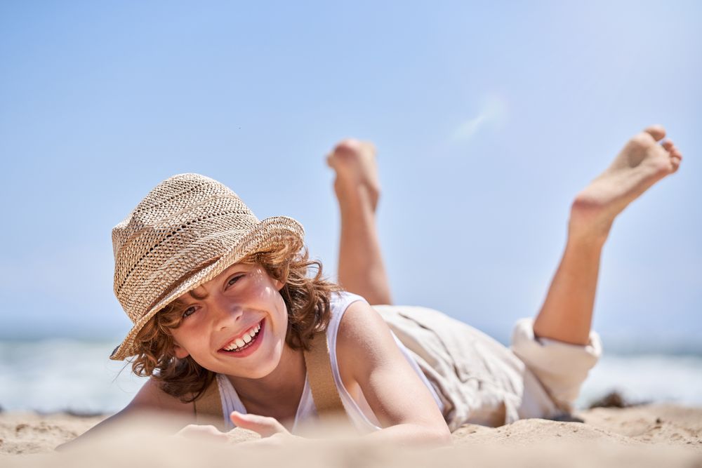 Happy boy lying on seashore and playing with sand
