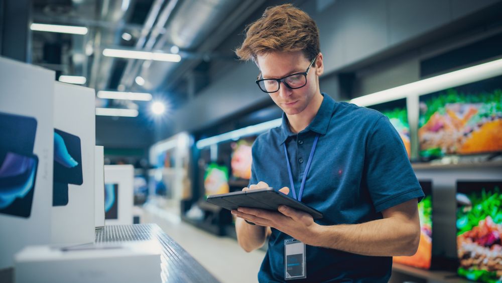 Portrait of Sales Representative in Home Electronics Store Using Tablet Computer for Online Workflow.