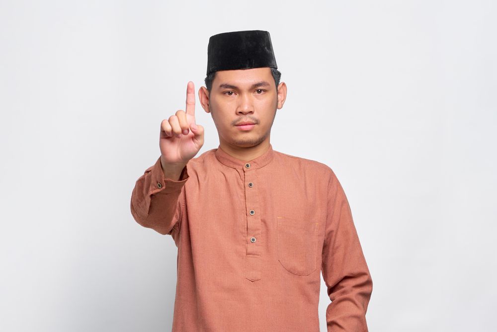 Muslim man in kufi hat with finger pointed up