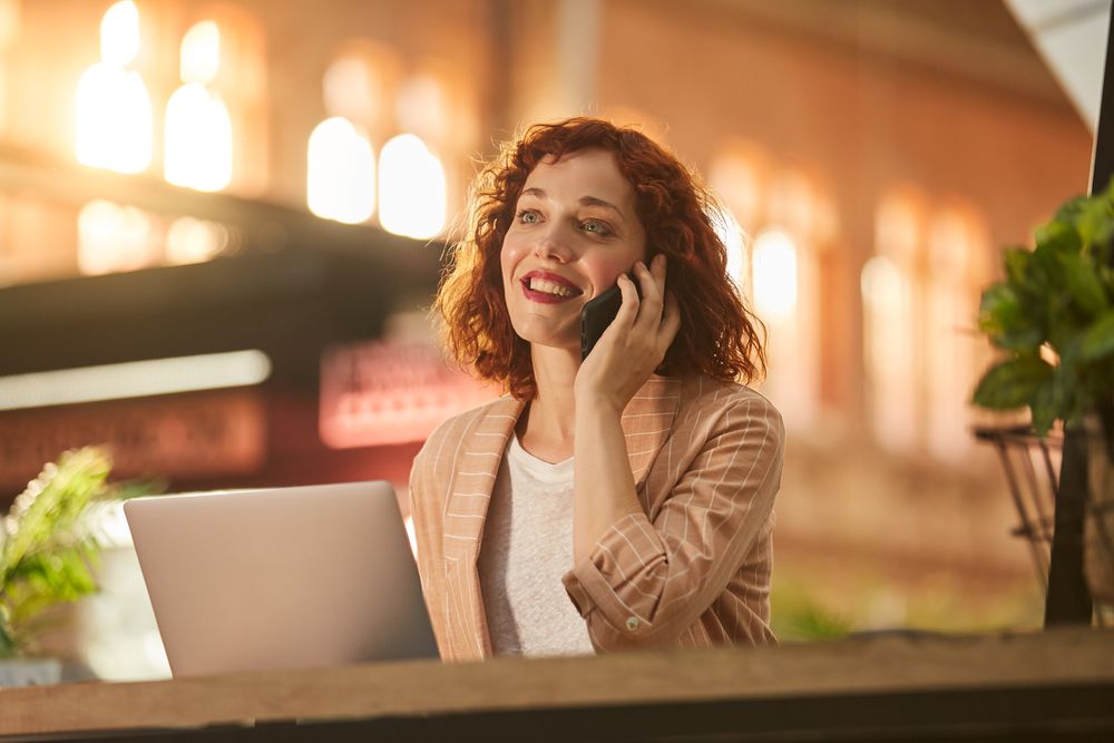 Young woman talking on phone while working on laptop