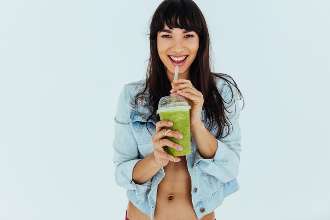 Portrait of beautiful woman drinking fresh green smoothie on light background