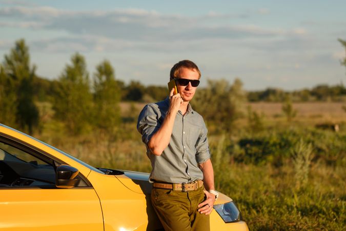 Male talking on his cell phone while leaning on side of stopped yellow car