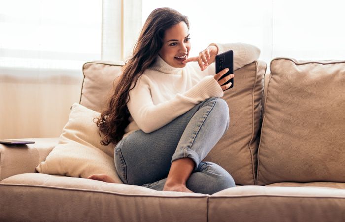 Connected at Home: Young Woman Sitting on Sofa Using Smartphone