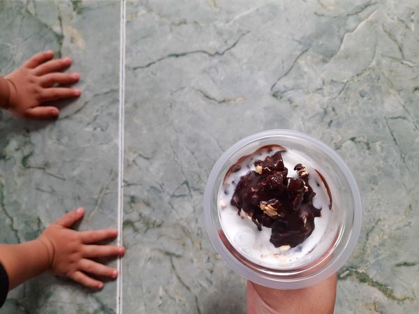 Vanilla Chocolate Ice Cream in Plastic Cup with Child’s Hands Reaching on Tiled Floor