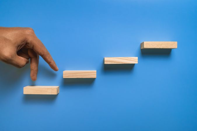 male hand walk on stairway wooden blocks isolated on blue background