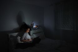 Mother and son using gadgets in bedroom at night