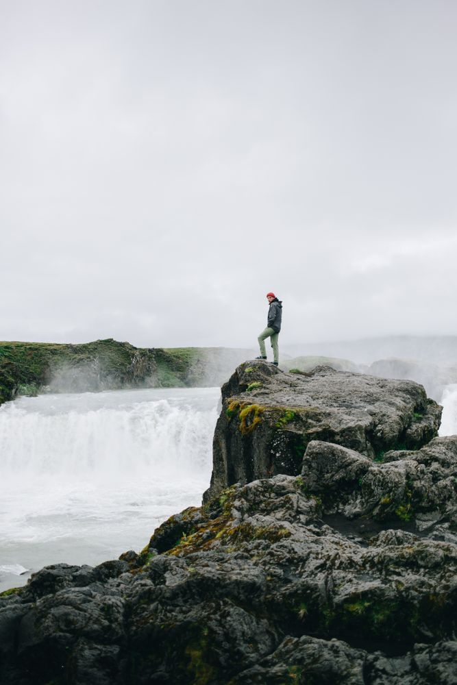 Man on rocky cliff over waterfall, vertical