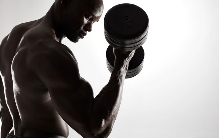 Fit man working out with dumbbells against grey background