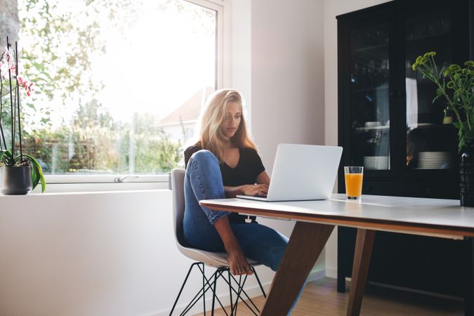 Young woman sitting in kitchen and working on laptop in morning