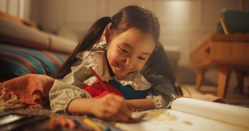 Evening Portrait of Cute Little Girl Drawing while Lying on the Floor in Living Room.