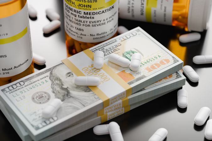 Prescription Medicine Bottles and Pills Next To Stacks of 100 Dollar Bills.