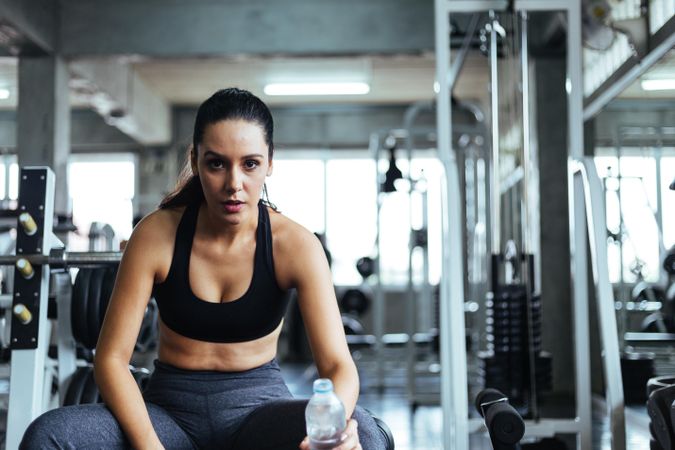 Woman sitting on bench in gym with water bottle