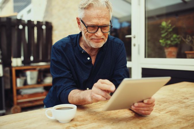 Mature man reading his tablet outside with a cup of coffee