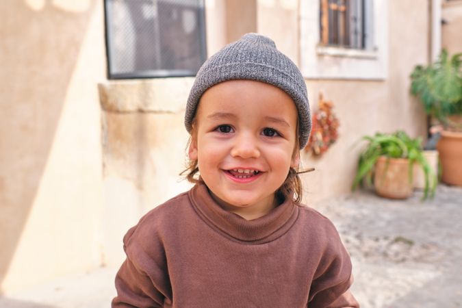 Joyful stylish toddler smiling at camera near old building in ba